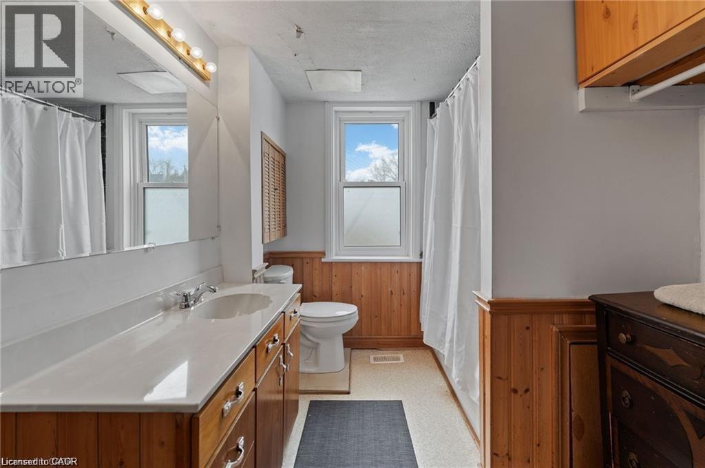 Full bathroom featuring a wood-finish vanity with a single sink and a broad countertop, a large wall-mounted mirror, and a wall-mounted light fixture - 2 Mill Street E, York, ON