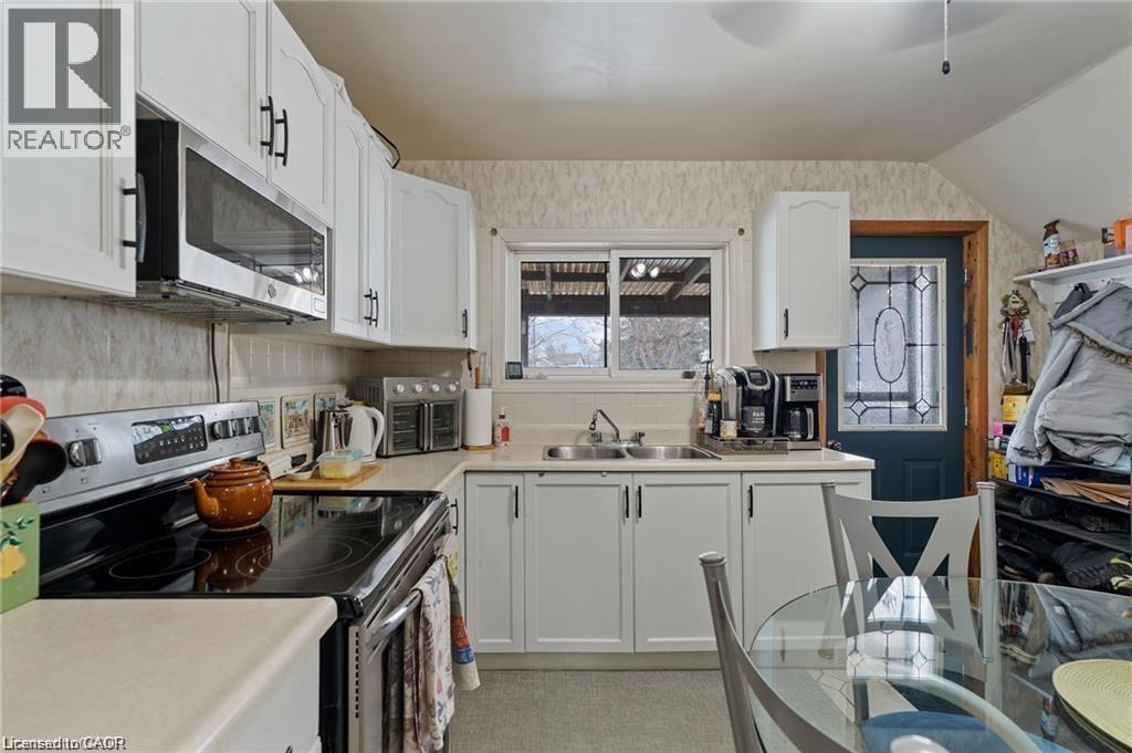 Kitchen featuring white cabinetry with black hardware, a stainless steel over-the-range microwave, a black electric range, a double basin sink, and a rear exterior door with decorative glass - 2 Mill Street E, York, ON