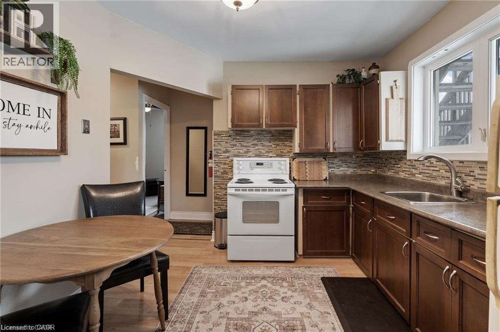 Kitchen featuring wood-finish flooring, dark wood cabinetry, a mosaic tile backsplash, and a stainless steel sink - 2 Mill Street E, York, ON