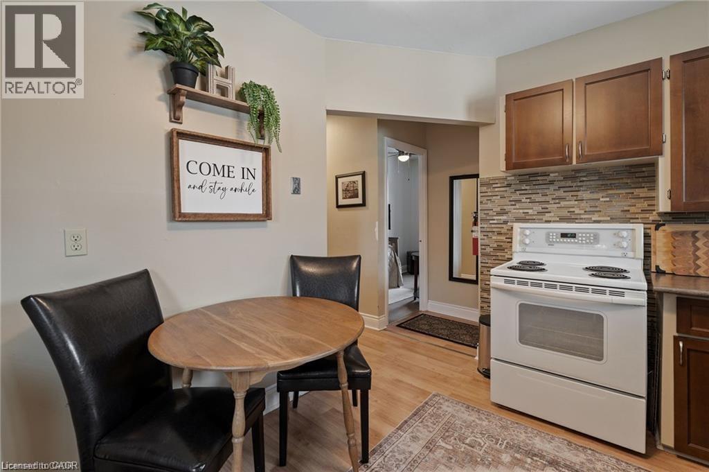Compact kitchen featuring wood-finish flooring, a white electric range, and a mosaic tile backsplash - 2 Mill Street E, York, ON