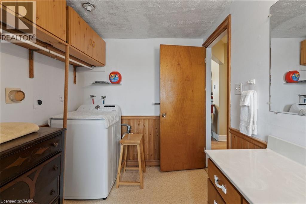 Dedicated laundry area featuring a top-load washing machine, wood-finish wall cabinetry, and beadboard wainscoting - 2 Mill Street E, York, ON