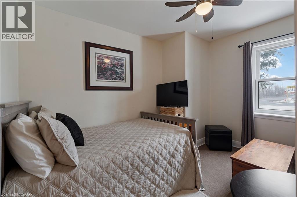 Bedroom featuring a double-hung window with a dark curtain rod, neutral wall paint, and a ceiling fan with integrated lighting - 2 Mill Street E, York, ON