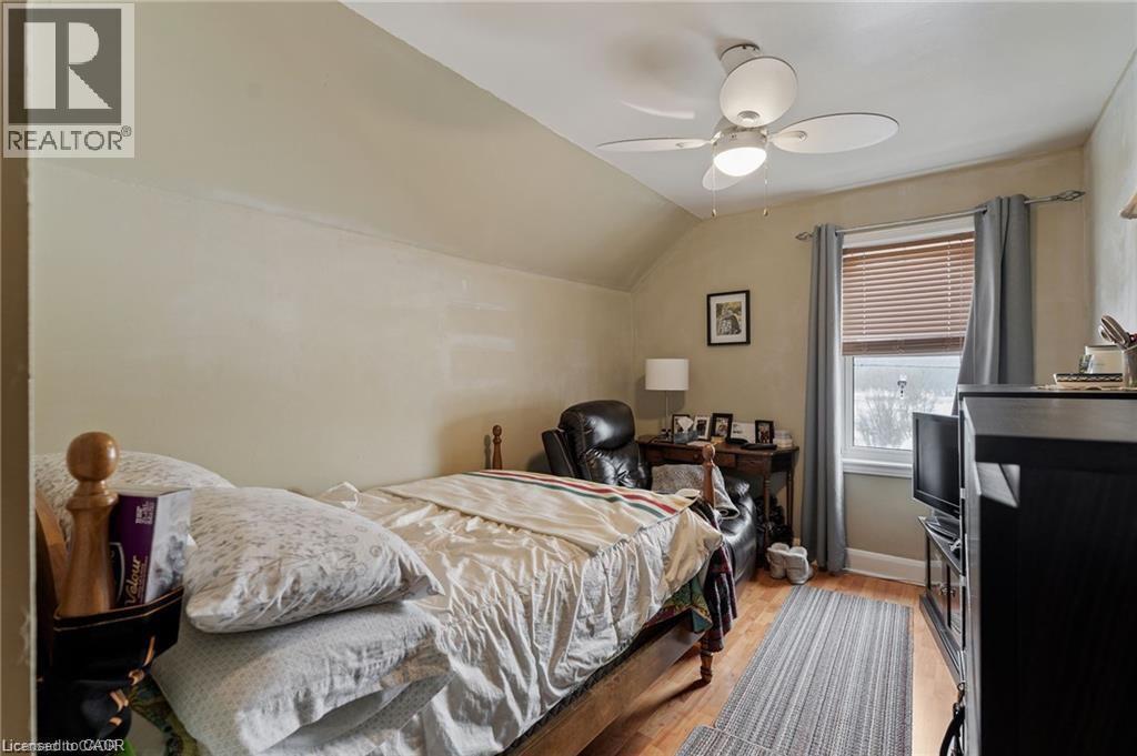 Room featuring wood-finish flooring, a window with horizontal blinds and curtains, a ceiling fan with integrated lighting, and sloped ceiling details - 2 Mill Street E, York, ON