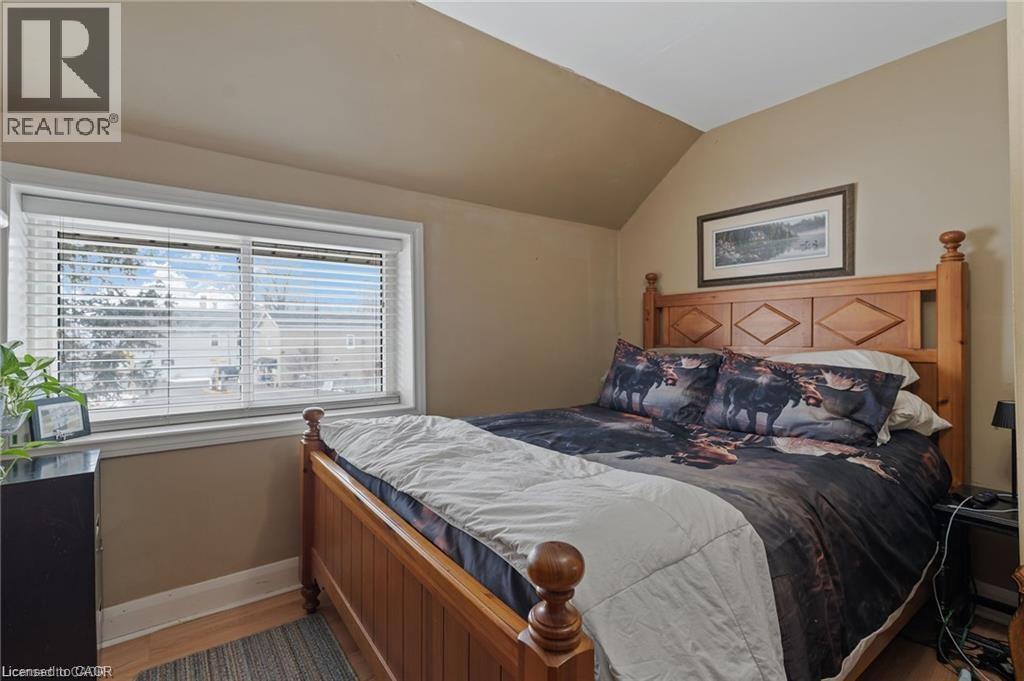 Bedroom featuring wood-finish flooring, a pitched ceiling, and a large window with white blinds - 2 Mill Street E, York, ON