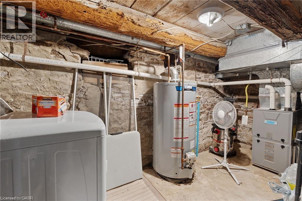 Basement utility area featuring exposed stone foundation walls, wood beam ceiling, and concrete flooring - 2 Mill Street E, York, ON