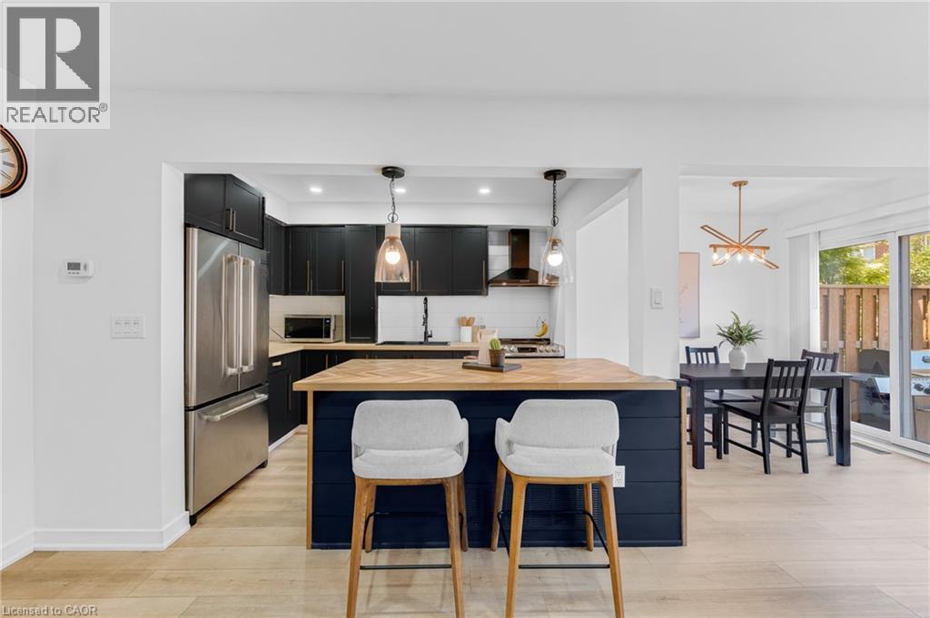 Modern kitchen with black cabinetry, stainless steel appliances, and a central island featuring a light wood countertop - 5275 Banting Court, Burlington, ON