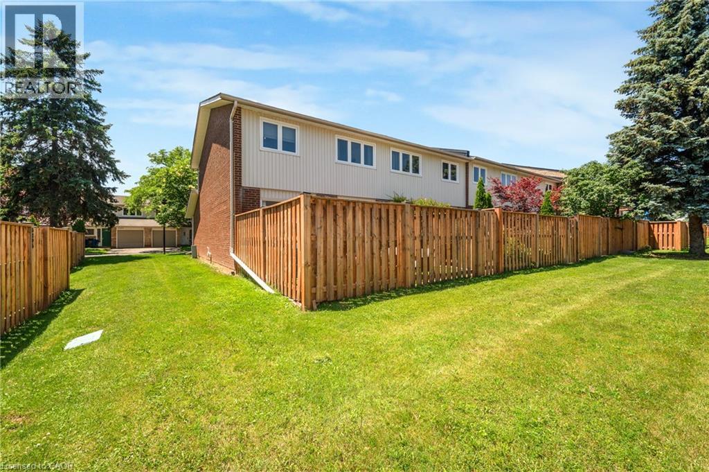 Expansive green lawn parcel framed by a wooden privacy fence, featuring a two-story residence with brick and siding exterior, multiple windows, and mature trees - 5275 Banting Court, Burlington, ON