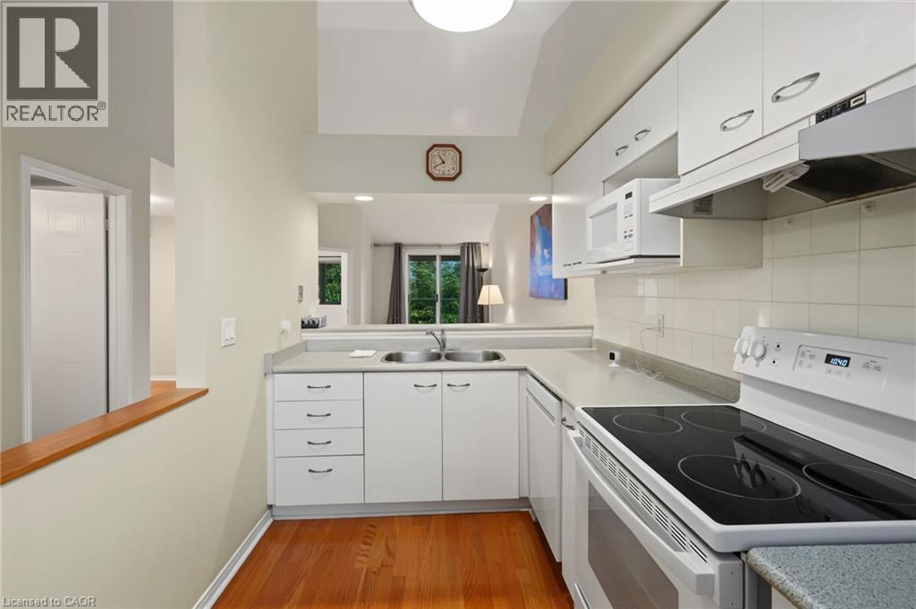Kitchen featuring wood-finish flooring, white cabinetry, a double basin sink, and a white electric range with overhead microwave - 117 E Bristol Road E Unit# 64, Mississauga, ON