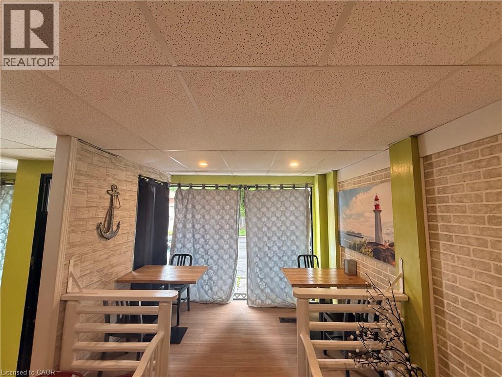 Recessed lighting illuminates the space, featuring wood-finish flooring, drop ceiling panels, and light-colored brick-style wall accents - 486 James Street N, Hamilton, ON