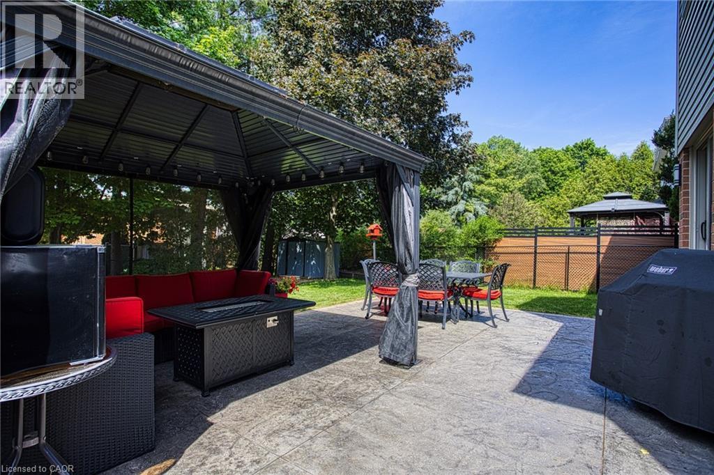 Expansive stamped concrete patio featuring a permanent gazebo with lighting, a privacy fence, and mature trees - 5 Shetland Drive, Waterdown, ON