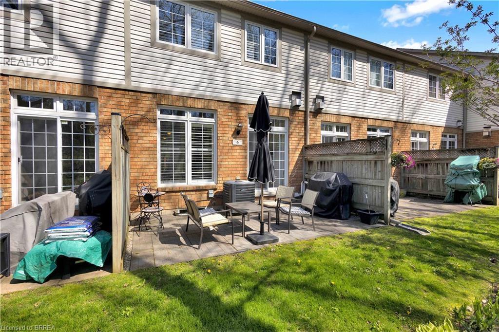 Patio area featuring brick and siding exterior, a sliding glass door, and multiple windows with white blinds - 120 Beddoe Drive Unit# 6, Hamilton, ON