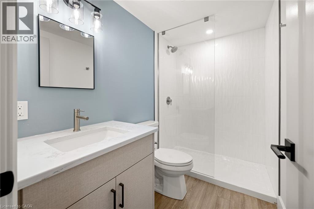 Full bathroom featuring a glass-enclosed shower, single vanity with integrated sink, wood-finish flooring, and contemporary light fixtures - 361 Coleridge Place, Waterloo, ON - Indoor Photo Showing Bathroom