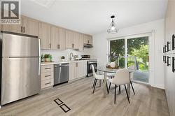 Modern kitchen featuring stainless steel appliances, light wood-finish cabinetry with matte black hardware, white countertops, and wood-finish flooring -
