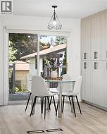 Eat-in kitchen area featuring a glass-top table, wood-finish flooring, full-height cabinetry with black pulls, and a geometric pendant light fixture -