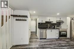 Compact kitchen featuring white cabinetry, stainless steel appliances, a matte black faucet, dark countertops, and wood-finish flooring -