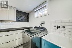 Laundry room featuring white shaker cabinetry, dark wood-finish countertops, subway tile backsplash, and a utility sink with wall-mounted black fixtures -
