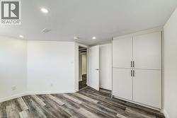 Room featuring wood-finish flooring, recessed lighting, white walls, and built-in cabinetry with dark hardware -