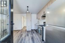 Open concept kitchen featuring wood-finish flooring, light wood-finish cabinetry, stainless steel appliances, and a gas range -