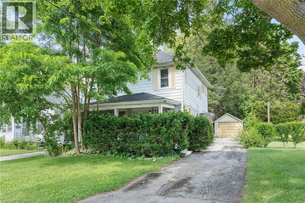 White siding residence with a covered porch, set on a property featuring mature trees and a detached garage - 35 Basil Avenue, Simcoe, ON