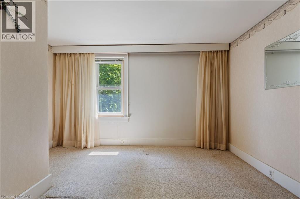 Room featuring a double-hung window with a tree canopy backdrop, wall-to-wall carpeting, and neutral-toned wallpaper - 35 Basil Avenue, Simcoe, ON