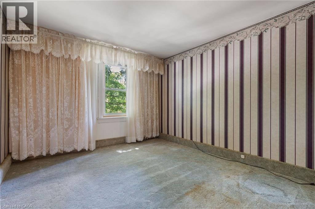 Room featuring a window with lace curtains, wall-to-wall carpeting, and striped wallpaper with a decorative border - 35 Basil Avenue, Simcoe, ON