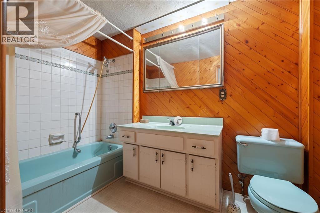 Bathroom featuring natural wood paneling, a light blue bathtub, and white tiled shower surround - 35 Basil Avenue, Simcoe, ON