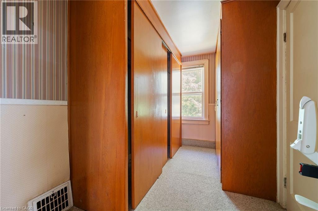 Hallway featuring wood-finish closet doors, patterned wallpaper, and a window with exterior views - 35 Basil Avenue, Simcoe, ON
