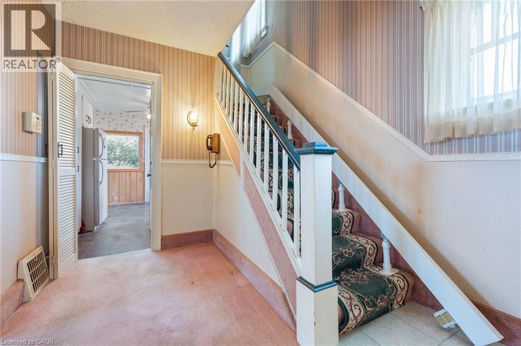 Staircase with an ornate carpet runner, white balusters, and a dark newel post - 35 Basil Avenue, Simcoe, ON