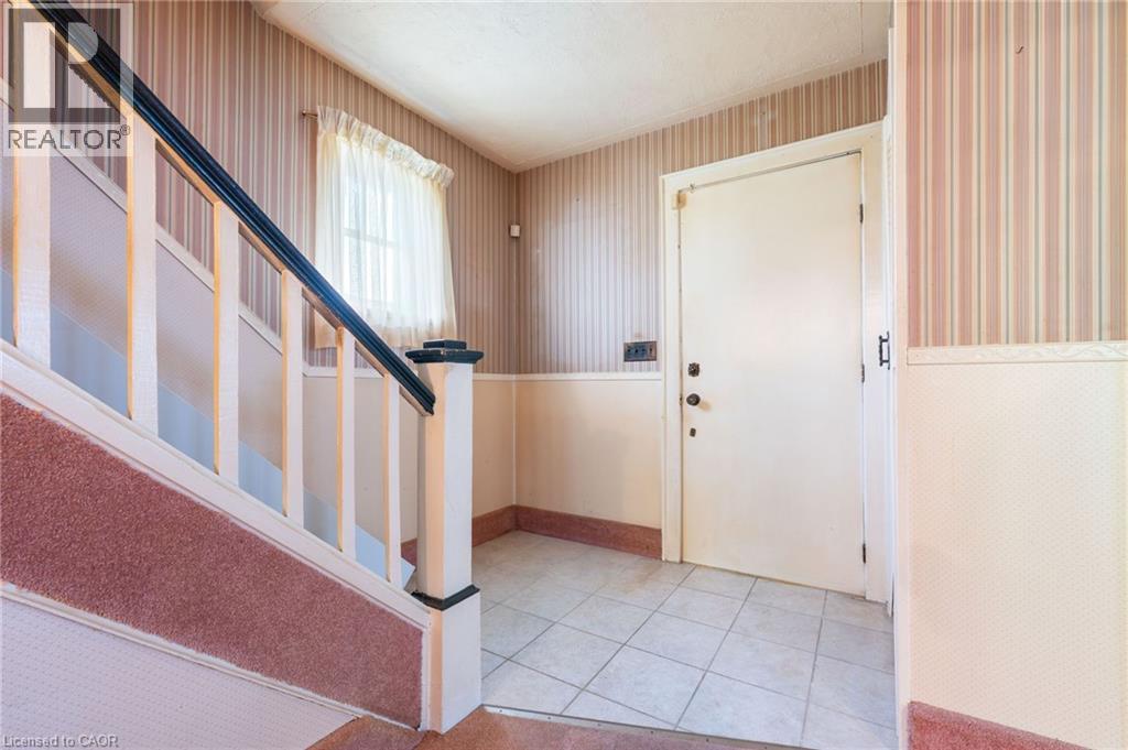 Entryway featuring a white paneled door, light-colored tile flooring, and a staircase with a black handrail and carpeted treads - 35 Basil Avenue, Simcoe, ON