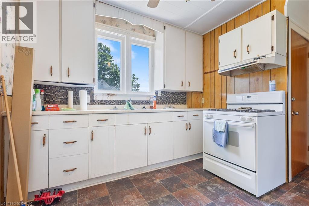 Kitchen featuring white cabinetry with brass-tone hardware, a white range, and a mosaic tile backsplash - 35 Basil Avenue, Simcoe, ON