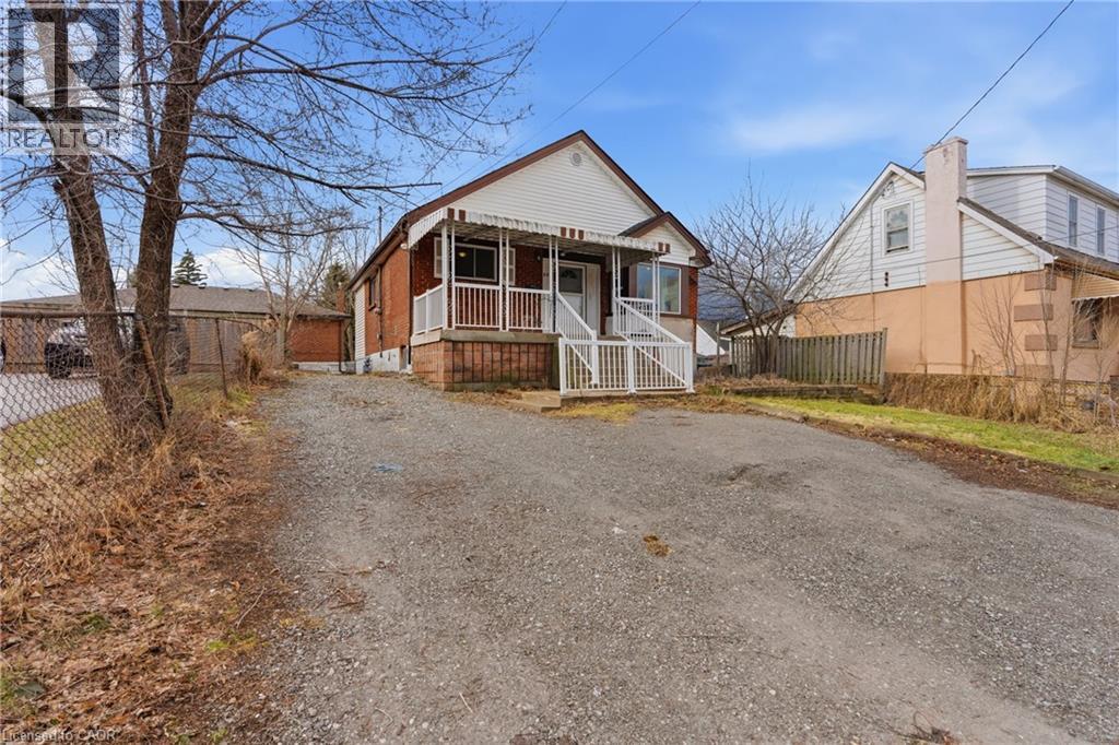 Brick and siding home featuring a covered front porch with white railings, a gravel driveway, and a chain-link fence - 880 Lawrence Road, Hamilton, ON