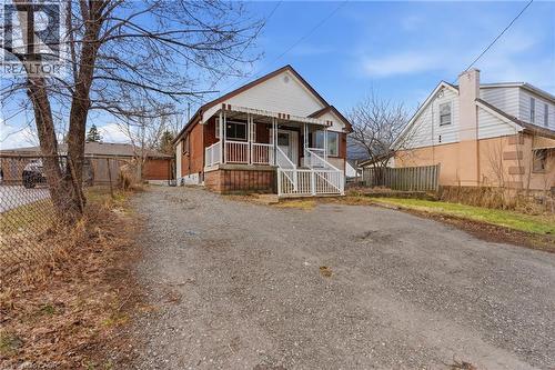 Brick and siding home featuring a covered front porch with white railings, a gravel driveway, and a chain-link fence - 880 Lawrence Road, Hamilton, ON 