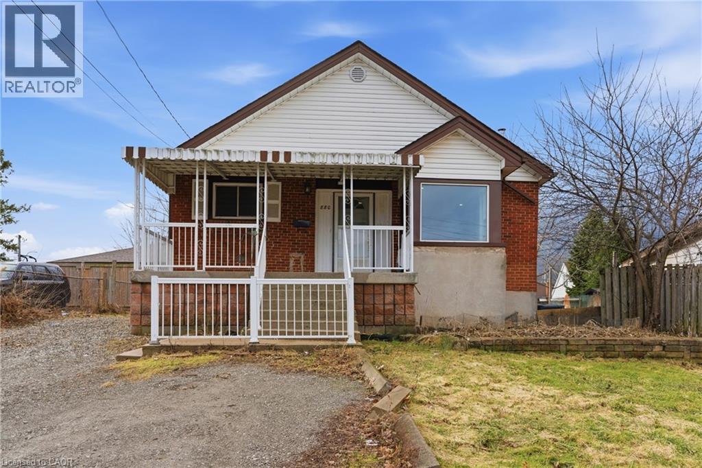 Brick and siding exterior featuring a covered front porch with white railings, a front-facing gable, a bay window, and a gravel driveway - 880 Lawrence Road, Hamilton, ON