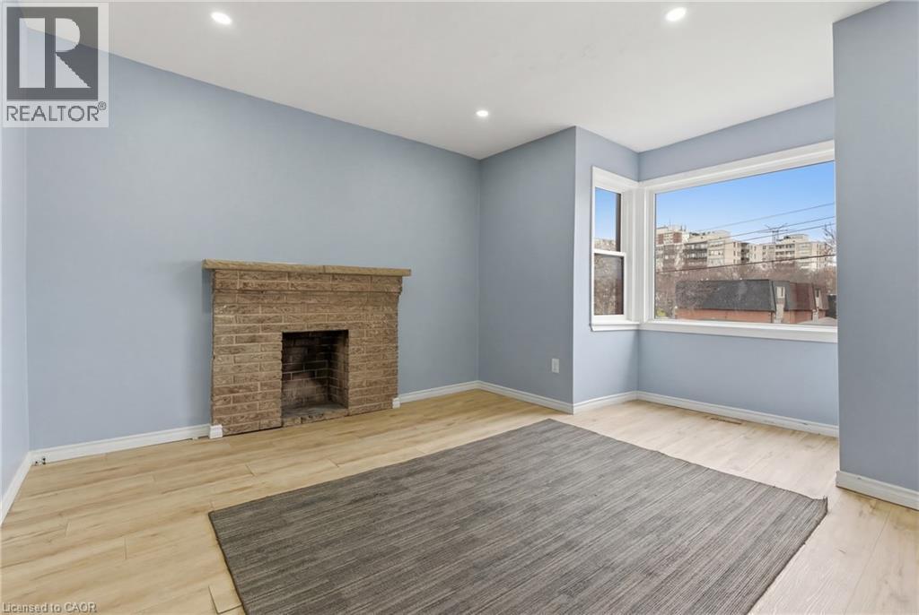 Spacious room featuring a brick fireplace, light wood-finish flooring, and recessed ceiling lighting - 880 Lawrence Road, Hamilton, ON