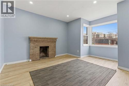 Spacious room featuring a brick fireplace, light wood-finish flooring, and recessed ceiling lighting - 880 Lawrence Road, Hamilton, ON 