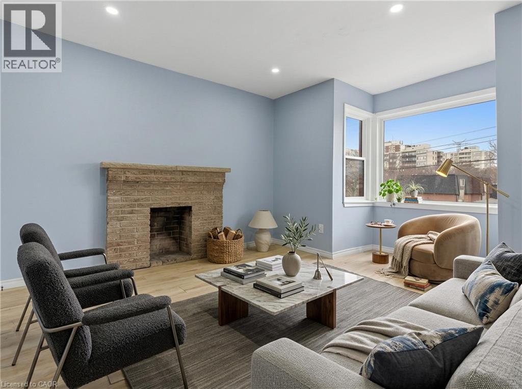 Living area featuring a brick fireplace with a stone mantel, light wood-finish flooring, a large corner window, recessed lighting, and light blue wall tones - 880 Lawrence Road, Hamilton, ON