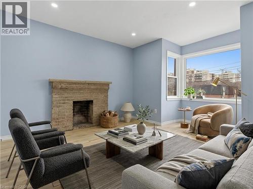 Living area featuring a brick fireplace with a stone mantel, light wood-finish flooring, a large corner window, recessed lighting, and light blue wall tones - 880 Lawrence Road, Hamilton, ON 