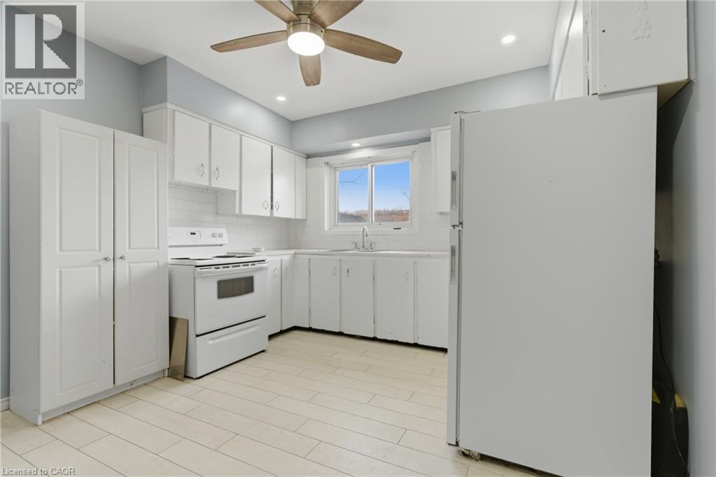 Kitchen featuring extensive white cabinetry, tile backsplash, white appliances, and a wood-finish ceiling fan with integrated lighting - 880 Lawrence Road, Hamilton, ON