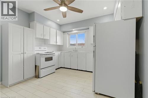 Kitchen featuring extensive white cabinetry, tile backsplash, white appliances, and a wood-finish ceiling fan with integrated lighting - 880 Lawrence Road, Hamilton, ON 