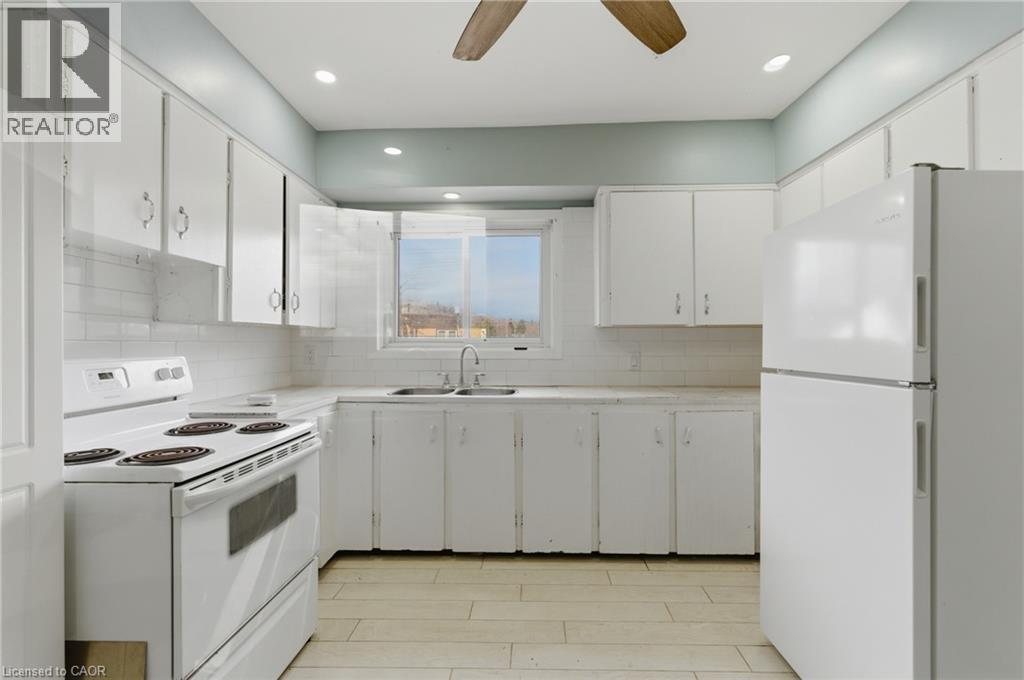 Kitchen featuring white cabinetry, white appliance suite, white subway tile backsplash, light-toned countertops, and wood-finish flooring - 880 Lawrence Road, Hamilton, ON