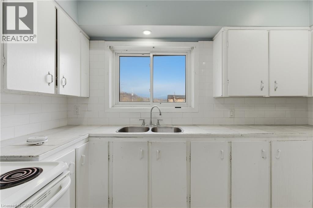 Kitchen featuring white cabinetry, white subway tile backsplash, a double basin stainless steel sink, and a white electric range - 880 Lawrence Road, Hamilton, ON