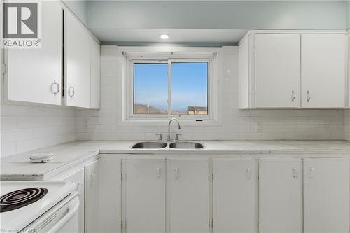 Kitchen featuring white cabinetry, white subway tile backsplash, a double basin stainless steel sink, and a white electric range - 880 Lawrence Road, Hamilton, ON 