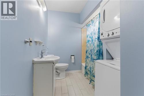 Bathroom featuring a corner vanity with integrated sink, toilet, tub with shower, and stacked laundry appliances - 880 Lawrence Road, Hamilton, ON 