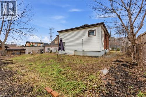 Expansive rear yard with a large grassy area, chain-link fencing, mature trees, and a visible side entrance to the dwelling - 880 Lawrence Road, Hamilton, ON 