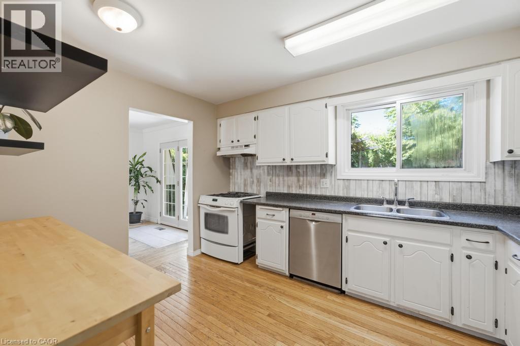 Kitchen featuring wood-finish flooring, white cabinetry with black hardware, dark countertops, and a stainless steel dishwasher - 14 Gateway Drive, Guelph, ON