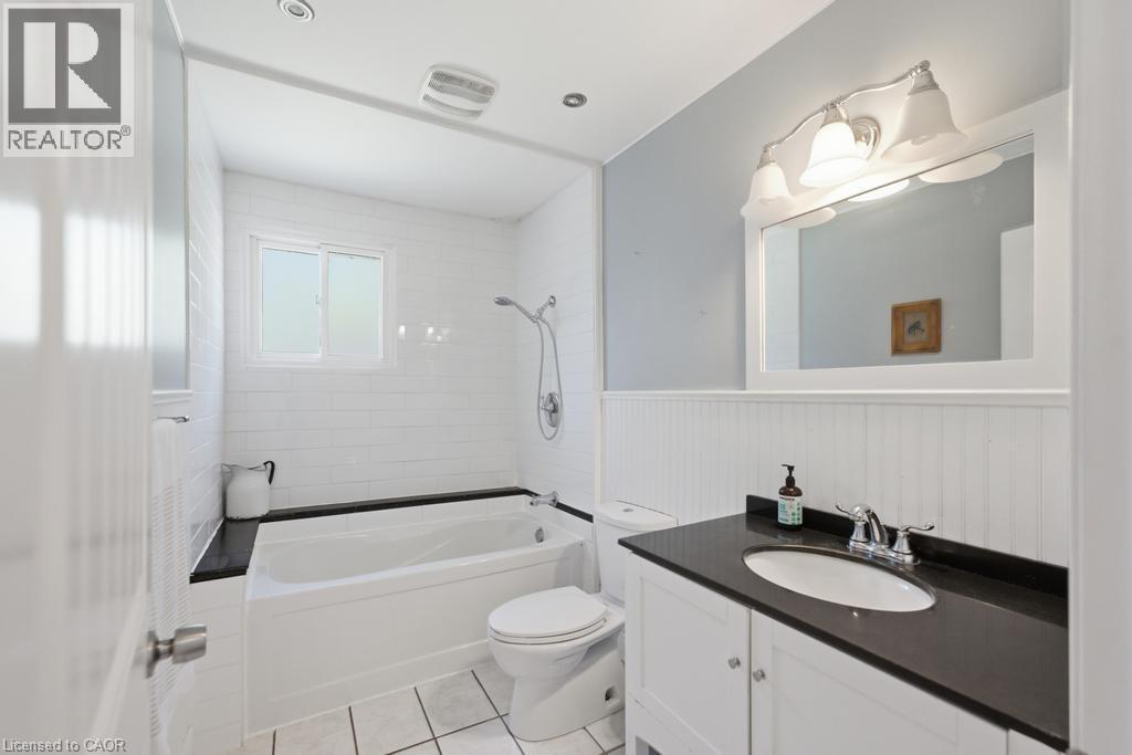 White bathroom featuring a built-in tub with black surround, a white vanity with a dark countertop and undermount sink, white subway tile shower walls, and beadboard wainscoting - 14 Gateway Drive, Guelph, ON