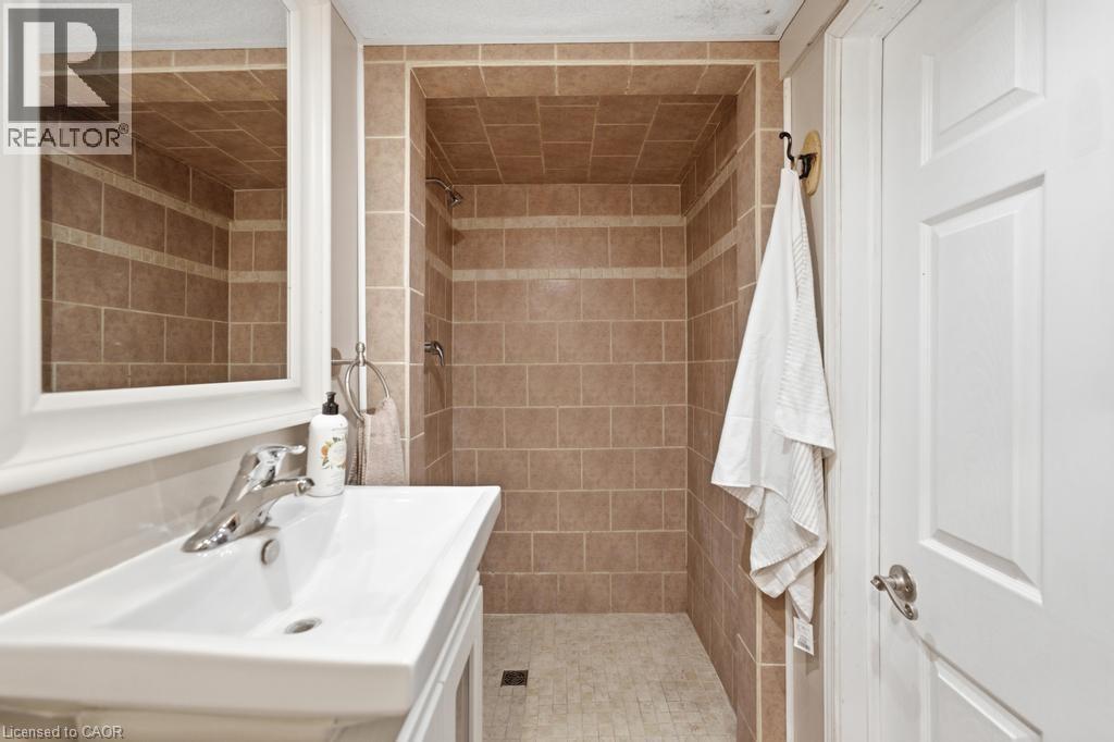 Bathroom featuring a tiled shower stall with a mosaic floor, a white vanity with an integrated sink, a chrome faucet, and a framed wall mirror - 14 Gateway Drive, Guelph, ON