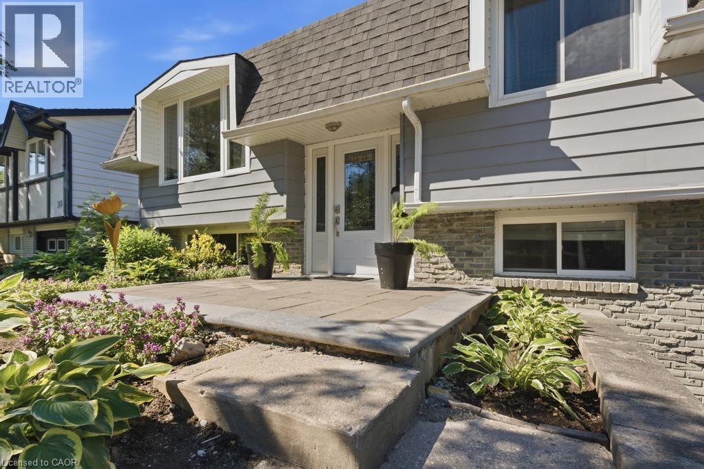 Split-level exterior featuring light grey siding, a stone facade, and a prominent front entrance with a full-light door - 14 Gateway Drive, Guelph, ON