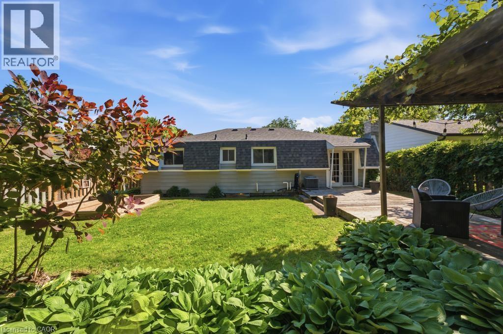 Expansive backyard featuring a manicured lawn, a raised wood-finish deck, and a distinct pergola-covered patio with brick accents - 14 Gateway Drive, Guelph, ON
