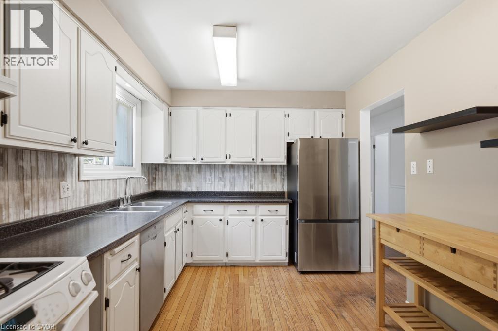 Kitchen featuring white cabinetry, dark countertops, wood-finish flooring, stainless steel appliances, and a window above the sink - 14 Gateway Drive, Guelph, ON
